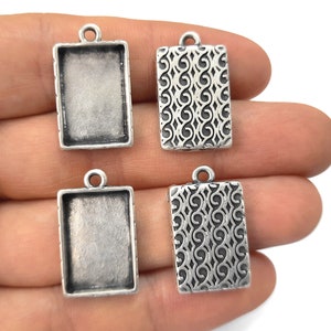 May include: Four silver-toned pendant trays, two with a decorative swirl pattern and two with a blank surface, ready for crafting.