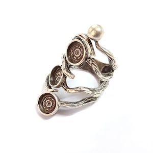 May include: A silver-toned ring with an abstract design. The ring features a series of circular settings and a small sphere, all connected by twisted, branch-like elements. The ring is set against a white background.
