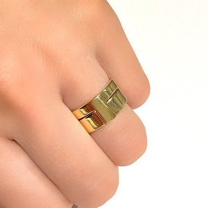 May include: A gold-toned ring with a unique interlocking design. The ring is worn on a finger.