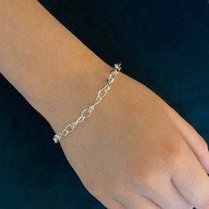 Puede incluir: Un brazalete de cadena de plata con un diseño delicado y trenzado.