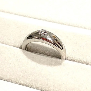 Puede incluir: Un anillo de banda de plata con un solo diamante pequeño y claro engastado en el centro.