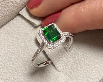 May include: A silver ring with a large emerald green gemstone surrounded by a halo of smaller clear gemstones.