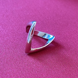 Könnte beinhalten: Ein silberner Ring mit einem V-förmigen Design. Der Ring ist an einer Seite offen und hat eine glatte, polierte Oberfläche.