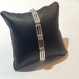 Peut inclure: Un bracelet en argent avec plusieurs rang&eacute;es de barres reli&eacute;es. Le bracelet est pr&eacute;sent&eacute; sur un coussin noir.