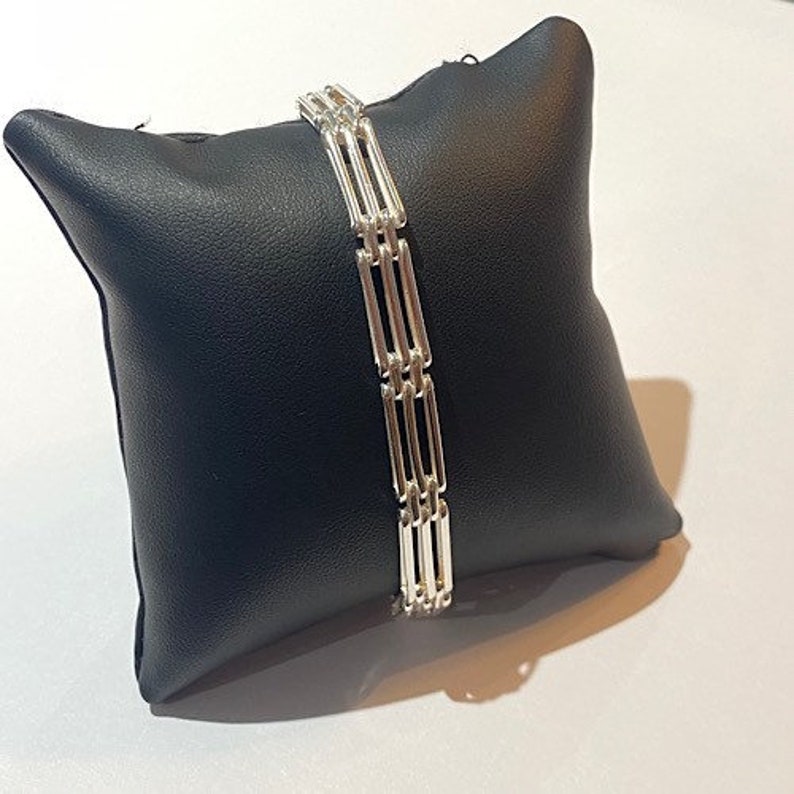 Peut inclure: Un bracelet en argent avec plusieurs rang&eacute;es de barres reli&eacute;es. Le bracelet est pr&eacute;sent&eacute; sur un coussin noir.