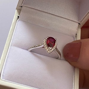 Peut inclure: Une bague de fiançailles en argent avec un rubis en forme de poire et un halo de diamants plus petits.
