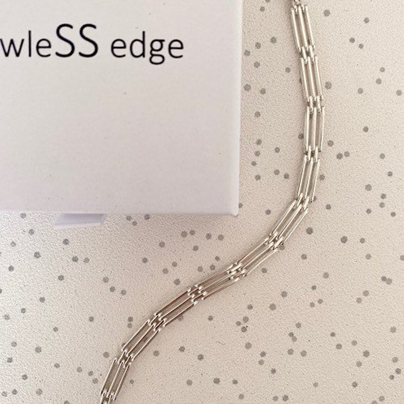 Peut inclure: Un collier en cha&icirc;ne argent avec une bordure sans couture. La cha&icirc;ne est compos&eacute;e de plusieurs maillons rectangulaires fins.