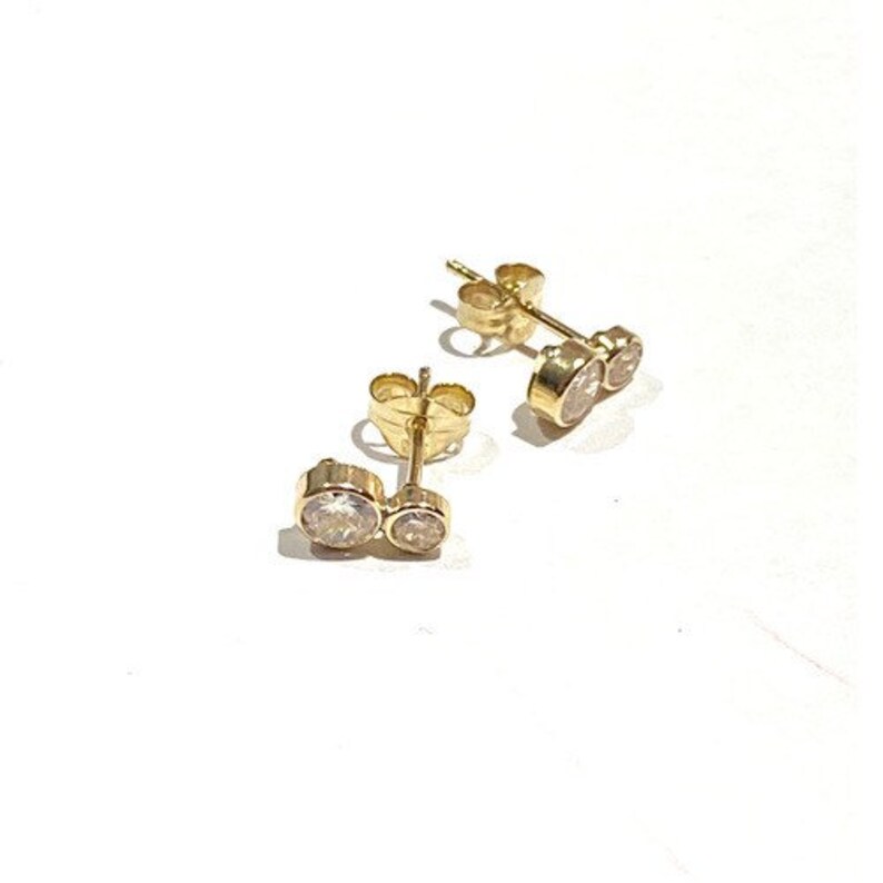 May include: A pair of gold earrings with two small round clear stones.