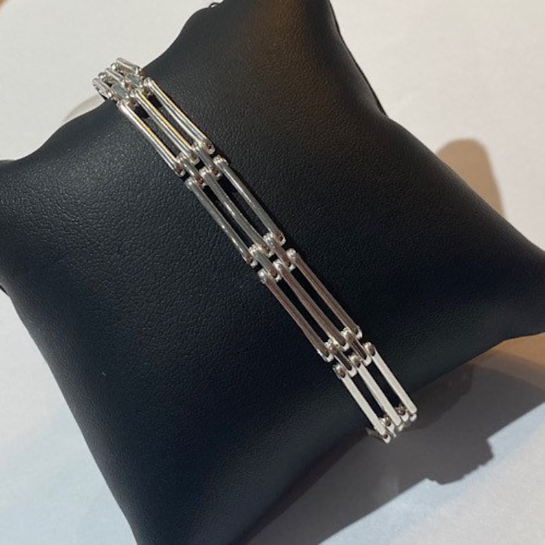 Peut inclure: Un bracelet en argent avec un design de cha&icirc;ne &agrave; maillons multiples. Le bracelet est compos&eacute; de plusieurs rang&eacute;es de barres reli&eacute;es.