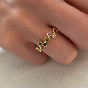 Peut inclure: Bague en or avec une rangée de pierres précieuses colorées. La bague est portée sur un doigt.