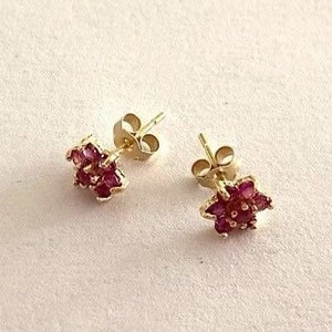 Może przedstawiać: Para złotych kolczyków w kształcie gwiazdy z czerwonymi rubinami.