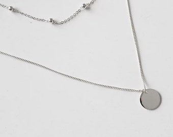 Op de afbeelding: Een zilveren gelaagde ketting met een delicate ketting en een dikkere ketting met een ronde hanger.