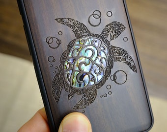 May include: A dark brown wooden phone case with a carved sea turtle design. The turtle's shell is inlaid with iridescent mother-of-pearl.