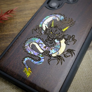 May include: A wooden phone case with a black dragon design inlaid with iridescent mother of pearl. The dragon is detailed with sharp claws and a fierce expression.