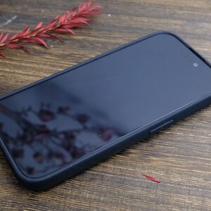 以下が含まれることがあります： 滑らかでマットな仕上がりの黒い携帯電話ケース。ケースは柔らかく柔軟な素材で作られており、画面の周りに傷から保護するための隆起した縁があります。