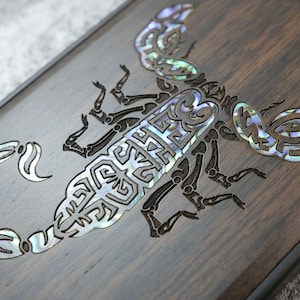May include: A dark brown wooden phone case with a detailed scorpion design inlaid with iridescent mother of pearl.