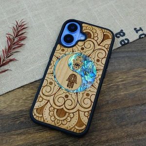 May include: A wooden phone case featuring a blue and white yin yang design and a mandala pattern. The case is crafted from wood and has a black border.