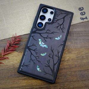 May include: A black phone case with a dark wood grain pattern and a design of a forest with bats. The phone case has a cutout for the camera lens and a black border.