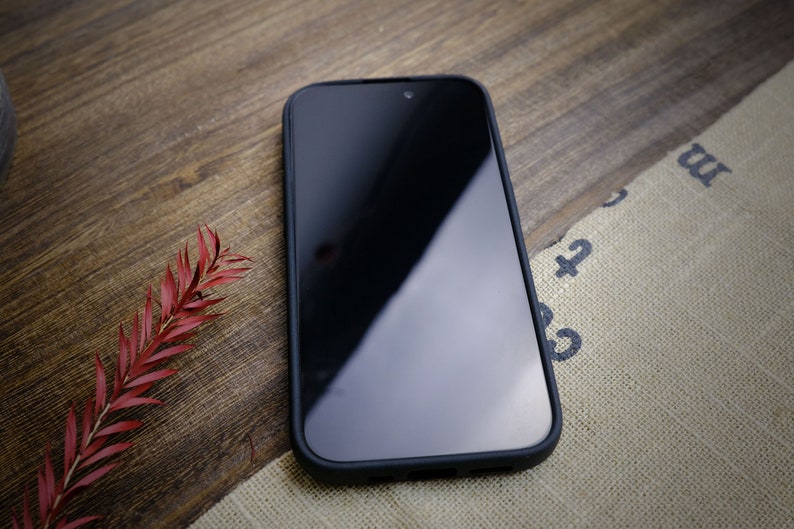 K&ouml;nnte beinhalten: Ein schwarzes Smartphone mit einem Displayschutz auf einer Holzoberfl&auml;che. Das Telefon befindet sich in einem schwarzen Etui.