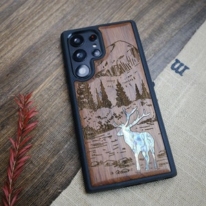 May include: A wooden phone case with a laser-engraved design of a mountain scene with a deer in the foreground. The deer is made of mother-of-pearl.