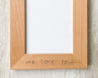 May include: A natural wood picture frame with a white mat. The top of the frame has the words "Papa" written in black marker with two hearts drawn next to it. The bottom of the frame has the words "we love you!" written in black marker.