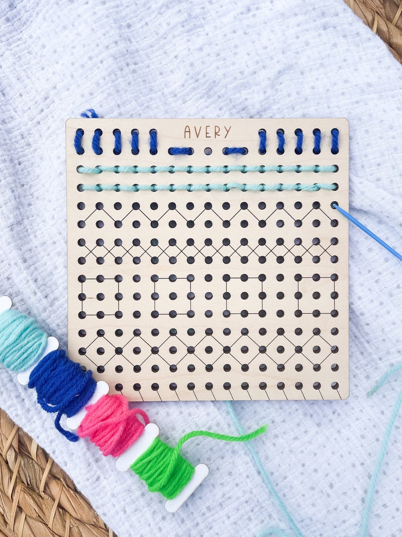 以下が含まれることがあります： 「AVERY」と印刷された木製の刺繍枠。枠には穴のグリッドがあり、縁取りされています。画像には、カラフルな糸の糸巻きがいくつかあります。