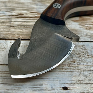 May include: A close-up of a silver hunting knife with a curved blade and a wooden handle. The knife has a hook on the back of the blade.