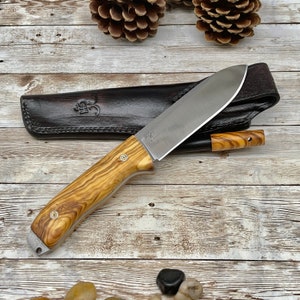 Pu&ograve; includere: Un fodero in pelle marrone con un coltello con manico in legno e lama in acciaio inossidabile. Il coltello ha una trama a grana di legno e un accento in ottone. Il fodero ha una chiusura a scatto.