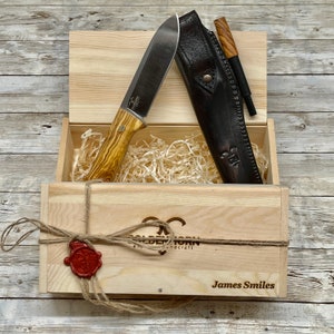 Pu&ograve; includere: Una scatola di legno con una custodia in pelle marrone e un coltello con manico in legno. La scatola &egrave; legata con uno spago e ha un sigillo di cera rossa. La scatola &egrave; incisa con il testo "Golden Morn" e "James Smiles".