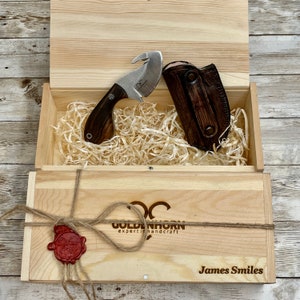 May include: A wooden box containing a brown leather sheath and a small knife with a brown wooden handle. The box is tied with twine and has a wax seal. The box is labelled "Goldenhorn expert in handcraft" and "James Smiles".