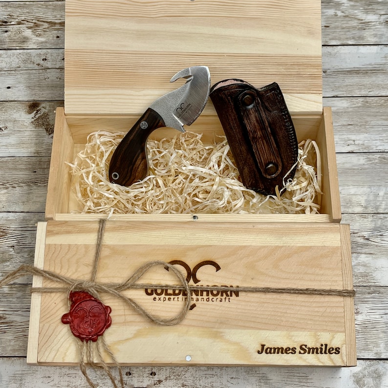 May include: A wooden box containing a brown leather sheath and a small knife with a brown wooden handle. The box is tied with twine and has a wax seal. The box is labelled "Goldenhorn expert in handcraft" and "James Smiles".