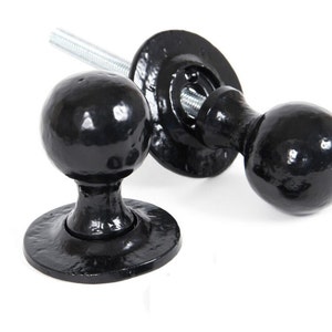 May include: Two black door knobs with round handles and a flat base. The knobs are made of metal and have a smooth finish.