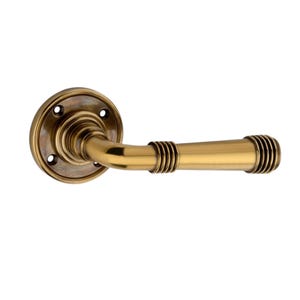 May include: A brass door handle with a circular backplate and a curved lever. The handle has a warm, golden colour and features decorative ribbed detailing on the lever. The design is classic and elegant, suitable for interior doors.