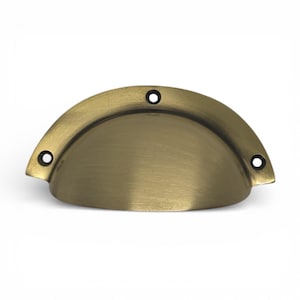 Może przedstawiać: Mosiężny uchwyt do szafki w kształcie półksiężyca z trzema otworami na śruby. Okucia mają szczotkowane wykończenie i lekkie zakrzywienie. Ten uchwyt w stylu vintage nadaje się do szuflad i szafek.