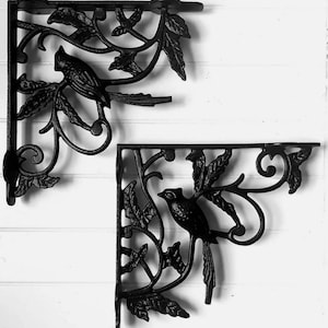 May include: Two black metal shelf brackets featuring a bird and leaf design. The brackets are ornate and have a vintage look.