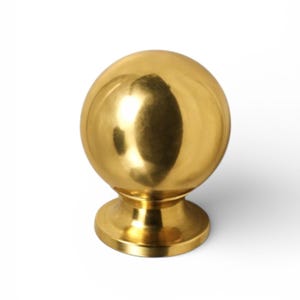 May include: A gold-colored, spherical cabinet knob with a polished finish. The knob has a round base and a smooth, reflective surface. This hardware is suitable for drawers, cabinets, or other furniture.