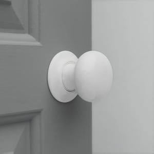 May include: A white, spherical door knob with a circular backplate, mounted on a grey door. A section of a white door is visible in the background. The door knob is a classic design, often found in homes.