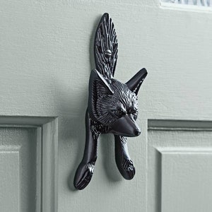 Könnte beinhalten: Schwarzer, detaillierter Türklopfer aus Metall in Form eines Fuchses. Der Fuchs ist in einer hockenden Position mit dem Kopf zur Seite gedreht.