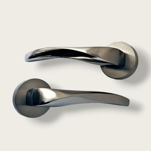 Può includere: Due maniglie per porte cromate lucide. Ogni maniglia presenta un design curvo e attorcigliato e una base circolare. Le maniglie sono su uno sfondo bianco, evidenziando le loro superfici riflettenti e l'estetica moderna.