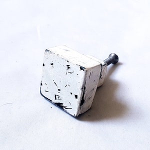 May include: White square cabinet knob with a black metal screw. The knob has a distressed finish with black paint accents.