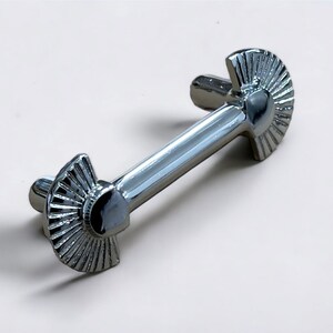 May include: A silver metal cabinet pull with a fan-shaped design on each end.