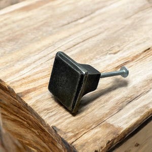 Peut inclure: Un bouton de porte carré en métal noir avec une vis argentée. Le bouton a une finition légèrement vieillie.