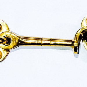 May include: A gold-toned metal hook and eye latch. The hook is attached to a long, straight bar with a rounded end. The eye is attached to a round plate with two holes.