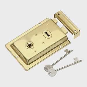 May include: A gold-colored, rectangular door lock with a keyhole and two keys. The lock has a rectangular plate with rounded edges and several screw holes. The keys are silver-colored with detailed key heads. The lock is designed for security.