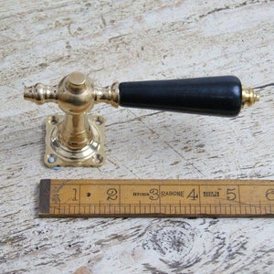 Peut inclure: Une poignée de porte en laiton avec un bouton en bois noir. La poignée a une base carrée et un design décoratif. Le bouton mesure environ 10 cm de long. La poignée est fabriquée en Angleterre.