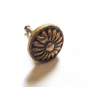 Op de afbeelding: Een kastknop van gietijzer met een decoratief bloemmotief. De knop is afgewerkt in een donker bronzen kleur.