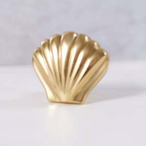 May include: A gold-coloured seashell-shaped decorative object. The seashell has a smooth, shiny surface and a detailed design.