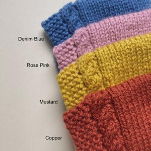 Puede incluir: Primer plano de cuatro muestras de tejido de punto en azul denim, rosa, mostaza y cobre. Los nombres de los colores est&aacute;n impresos en el lado izquierdo de la imagen. La textura de punto es visible, con un dise&ntilde;o de punto de cable en las muestras de mostaza y cobre.