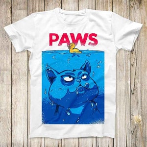 May include: White t-shirt with a blue cat submerged in water and a yellow rubber ducky floating above the water. The text "PAWS" is printed in red above the cat.