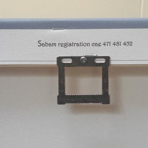May include: Close-up of the back of a canvas art piece. The canvas is white with a light blue border. A metal hanger is attached to the back. The text "Sabam registration cae 471 481 452" is printed on the canvas.